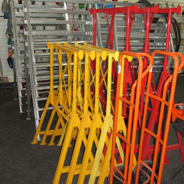 The image shows a collection of metal barriers, some yellow and others red, stacked in a warehouse or industrial setting. The barriers appear to be foldable, possibly used for crowd control or marking off restricted areas.